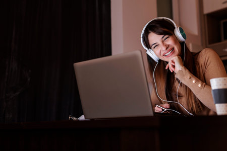 Beautiful young woman sitting in bed, relaxing at home in the morning, wearing headset listening to...