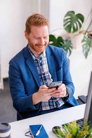 High angle view of modern businessman sitting at his desk in an office, smiling and typing text...