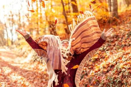 Beautiful young woman having fun spending sunny autumn day outdoors walking through a forest, holding an umbrella and jumpingの写真素材