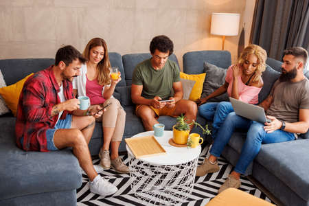 High angle view of group of friends sitting on couch and eating pizza while spending leisure time together at homeの写真素材