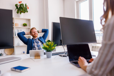 Business people working in a modern office, woman using smart phone and desktop computer while sitting at her deskの写真素材