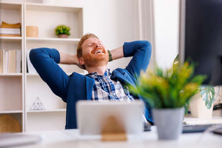 Confident successful businessman sitting at his desk taking a break and relaxing while working in an office, smiling and stretching outの写真素材
