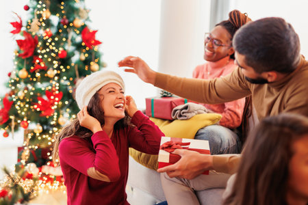 Group of cheerful young friends spending Christmas together at home, having fun exchanging and opening presentsの写真素材