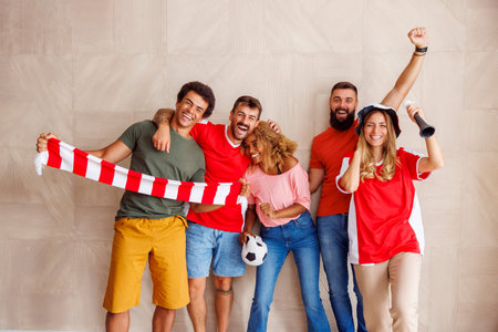 Group of cheerful football fans in sports jerseys with cheering props celebrating their team victory...
