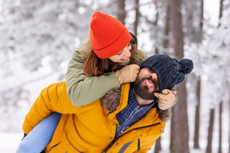 Beautiful young couple in love having fun spending winter vacation in the mountains, sitting and hugging in the snowの写真素材