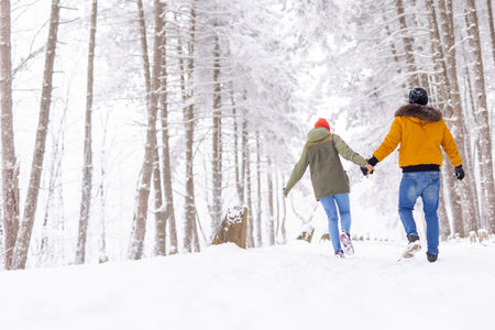 Couple having fun spending winter vacation in mountains holding hands and running in the snowの写真素材