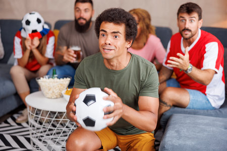 Group of friends watching football world championship game on TV at home, cheering, eating popcorn and drinking beer, dissapointed after their team missing the goalの写真素材