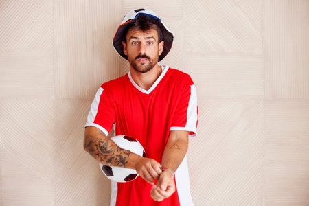 Male football fan wearing sports jersey holding soccer ball getting ready for the game, cheering and supporting his teamの写真素材