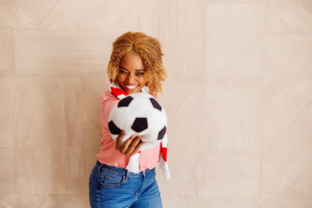 Portrait of cheerful female football fan holding soccer ball cheering and supporting her team while watching the gameの写真素材