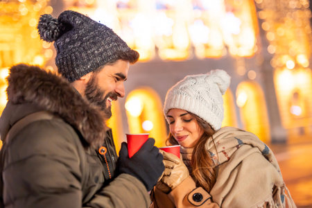 Couple in love having fun celebrating New Year in the city square, holding sparklers for midnight countdown with Christmas lights all aroundの写真素材
