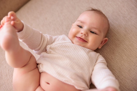 Top view of cute little baby boy lying in bed playing with his legs while mommy is changing his...