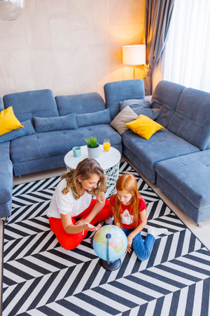 High angle view of beautiful mother and daughter having fun learning geography together at home, mother helping daughter explore the world map using globeの写真素材