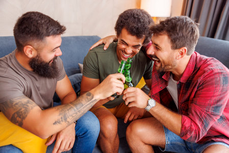 Group of male friends having fun spending leisure time together at home, making a toast and drinking beerの写真素材