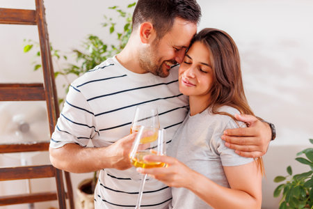Beautiful young couple in love celebrating moving in new apartment together, hugging and drinking wineの写真素材