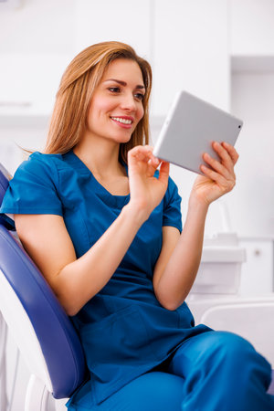 Female doctor wearing uniform sitting in ER using tablet computer checking patient's medical records and smiling with copy spaceの写真素材
