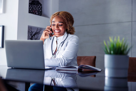 Young female online doctor having a phone conversation with patient using smart phone while working remotely from homeの写真素材