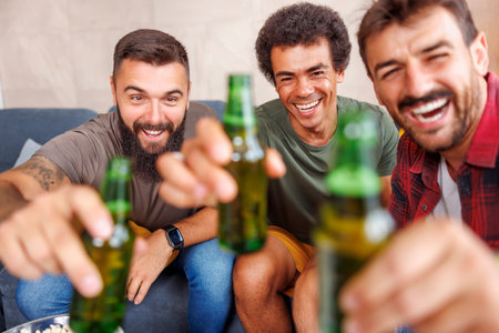 Group of male friends having fun spending leisure time together at home, making a toast and drinking beerの写真素材
