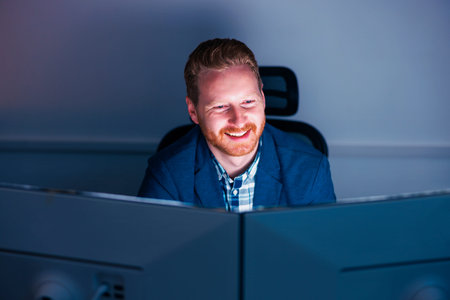 Confident successful businessman sitting at his desk using desktop computer while working late in an...