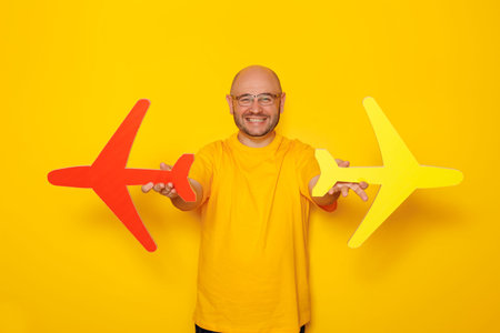 Portrait of man holding cardboard airplanes on yellow colored background - air travel and summer...