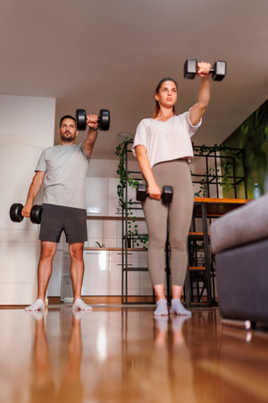 Active couple working out at home doing arms exercises lifting weightsの写真素材