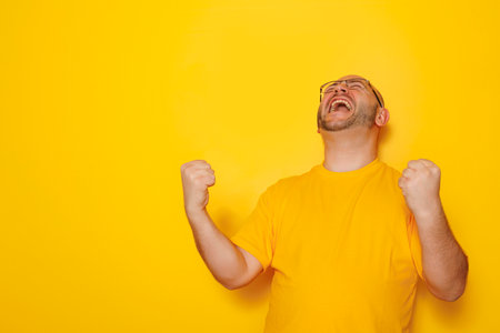 Portrait of cheerful funny mid 30s bald overweight man wearing yellow T-shirt and glasses cheering and celebrating isolated on yellow colored backgroundの写真素材