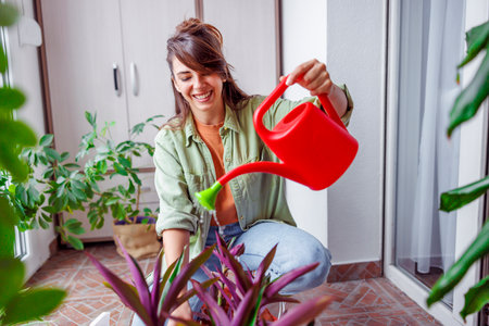 Beautiful young woman enjoying leisure time at home, relaxing while watering houseplantsの写真素材