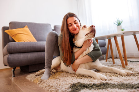 Beautiful young woman hugging and cuddling her pet dog while relaxing and enjoying leisure time at homeの写真素材
