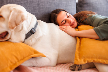 Woman relaxing at home taking an afternoon nap lying on the couch sleeping and hugging her pet dogの写真素材