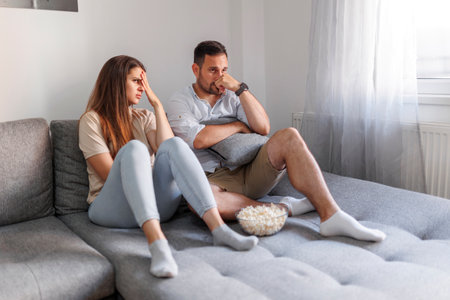 Beautiful young couple in love spending leisure time together at home, having fun watching horror movie on TV and eating popcornの写真素材