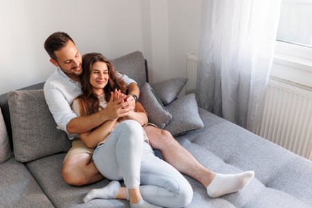 High angle view of a beautiful young couple in love relaxing at home, lying and hugging on the couchの写真素材