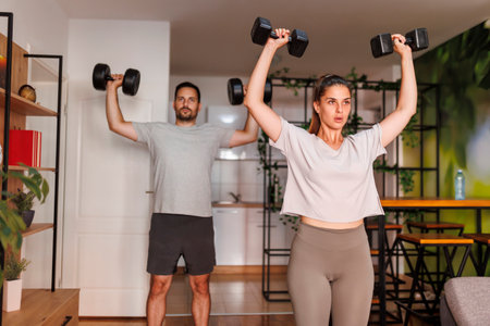 Active young couple doing biceps exercises using dumbbells while working out together at homeの写真素材