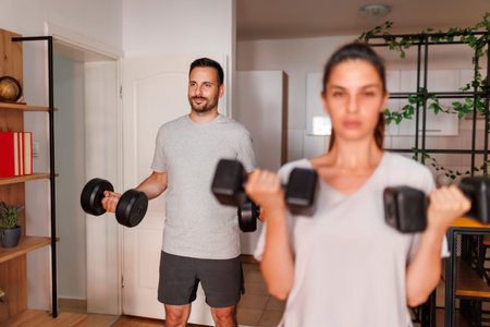 Active young couple lifting weights while working out together at home