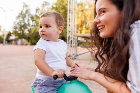 Beautiful young mother having fun spending leisure time outdoors with her cute little baby boy, teaching him how to ride a bikeの写真素材
