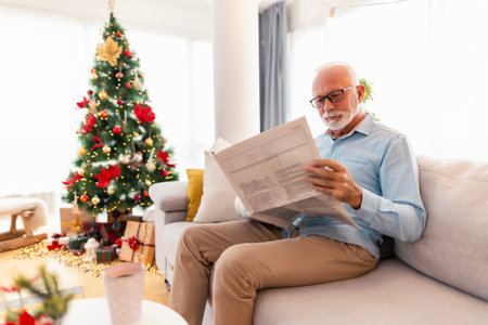 Senior man relaxing at home on Christmas morning, reading newspapers and drinking coffeeの写真素材