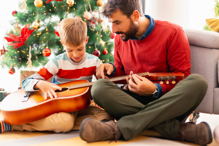 Father teaching son how to play the guitar while spending Christmas day together at homeの写真素材