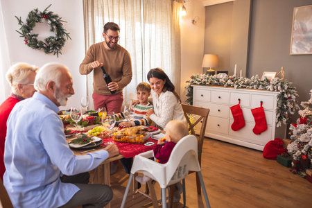 Beautiful happy family gathered around the table for Christmas dinner at home, opening a bottle of...