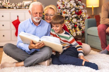 Grandparents showing old photo album to grandson while spending Christmas day together at home;...