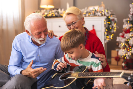 Little boy having fun spending winter holidays with grandparents, grandfather teaching grandson how to play the guitar on Christmas day at homeの写真素材