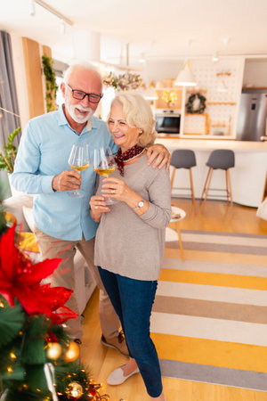 Happy senior couple relaxing at home while celebrating Christmas, hugging and drinking wine by nicely decorated Christmas treeの写真素材