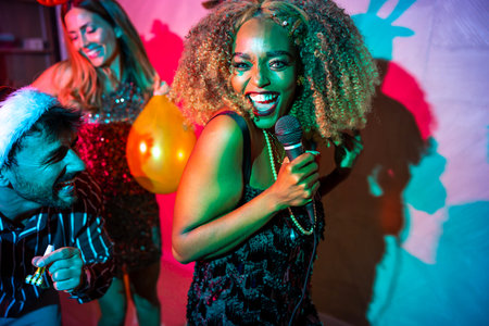 Group of cheerful young friends having fun singing karaoke and dancing at New Year's Eve party