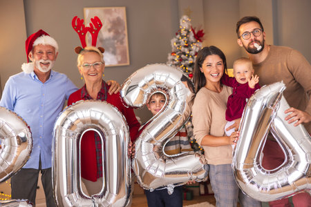 Beautiful happy multi-generation family celebrating Christmas at home, having fun holding giant balloons shaped as numbers 2024, representing the upcoming New Yearの写真素材