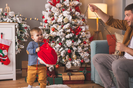 Cute little toddler boy having fun spending Christmas day at home with his father, playing, opening presents and decorating Christmas treeの写真素材