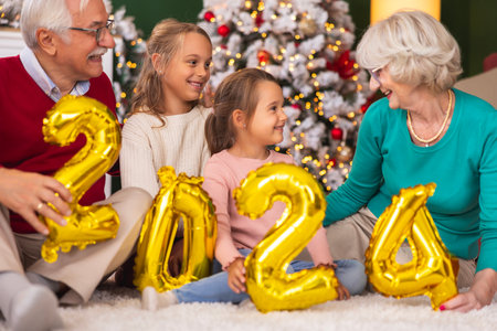 Beautiful happy multi-generation family having fun celebrating New Year at home, grandparents spending time with granddaughters, holding 2024 balloonsの写真素材