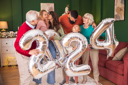 Beautiful happy family celebrating Christmas at home, having fun holding giant balloons shaped as numbers 2024, representing the upcoming New Yearの写真素材
