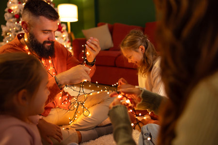 Parents and children having fun spending New Year's Eve together at home, sitting on the floor by the Christmas tree, playing with Christmas lightsの写真素材
