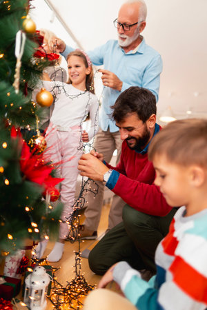 Beautiful happy multi-generation family gathered at home for winter holiday season celebration having fun decorating Christmas treeの写真素材