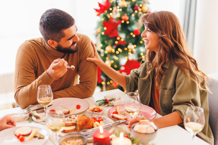 Beautiful young couple in love enjoying winter holiday season, having Christmas dinner with friends at homeの写真素材