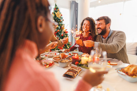 Group of cheerful young friends having Christmas dinner together at home, waving with sparklers and making a toast raising glasses of wineの写真素材