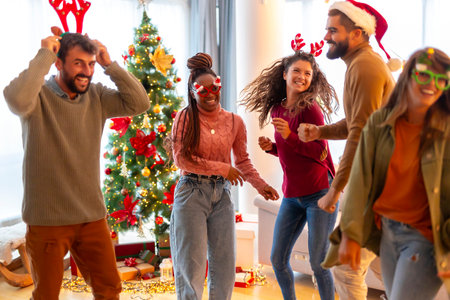 Group of young friends wearing Santa hats and costume reindeer antlers having fun singing and dancing while celebrating New Year at homeの写真素材