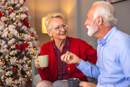 Happy senior couple drinking coffee and relaxing at home on Christmas morningの写真素材